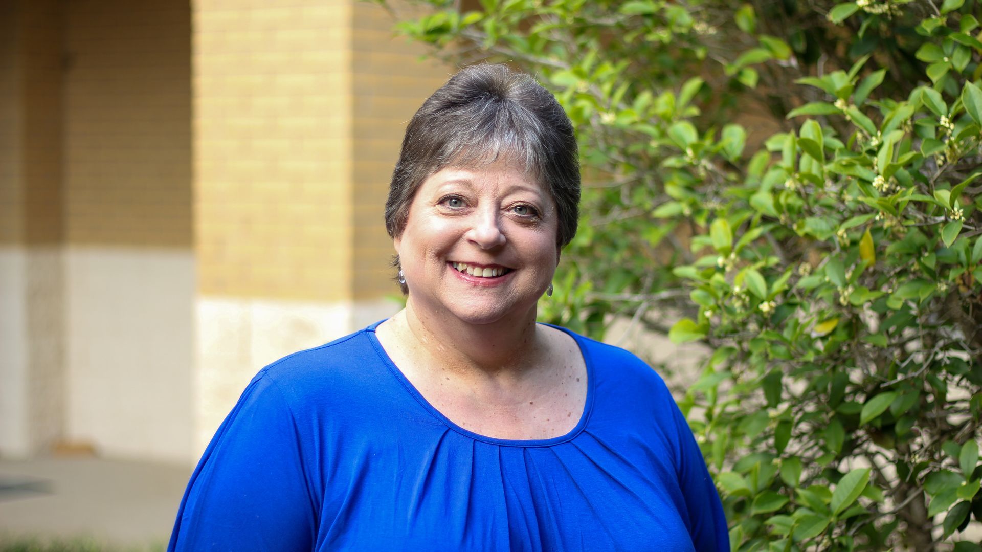 A woman is smiling in front of a church filled with wooden benches.