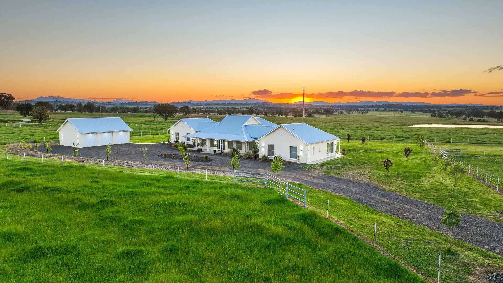 An aerial view of a house in the middle of a grassy field at sunset.