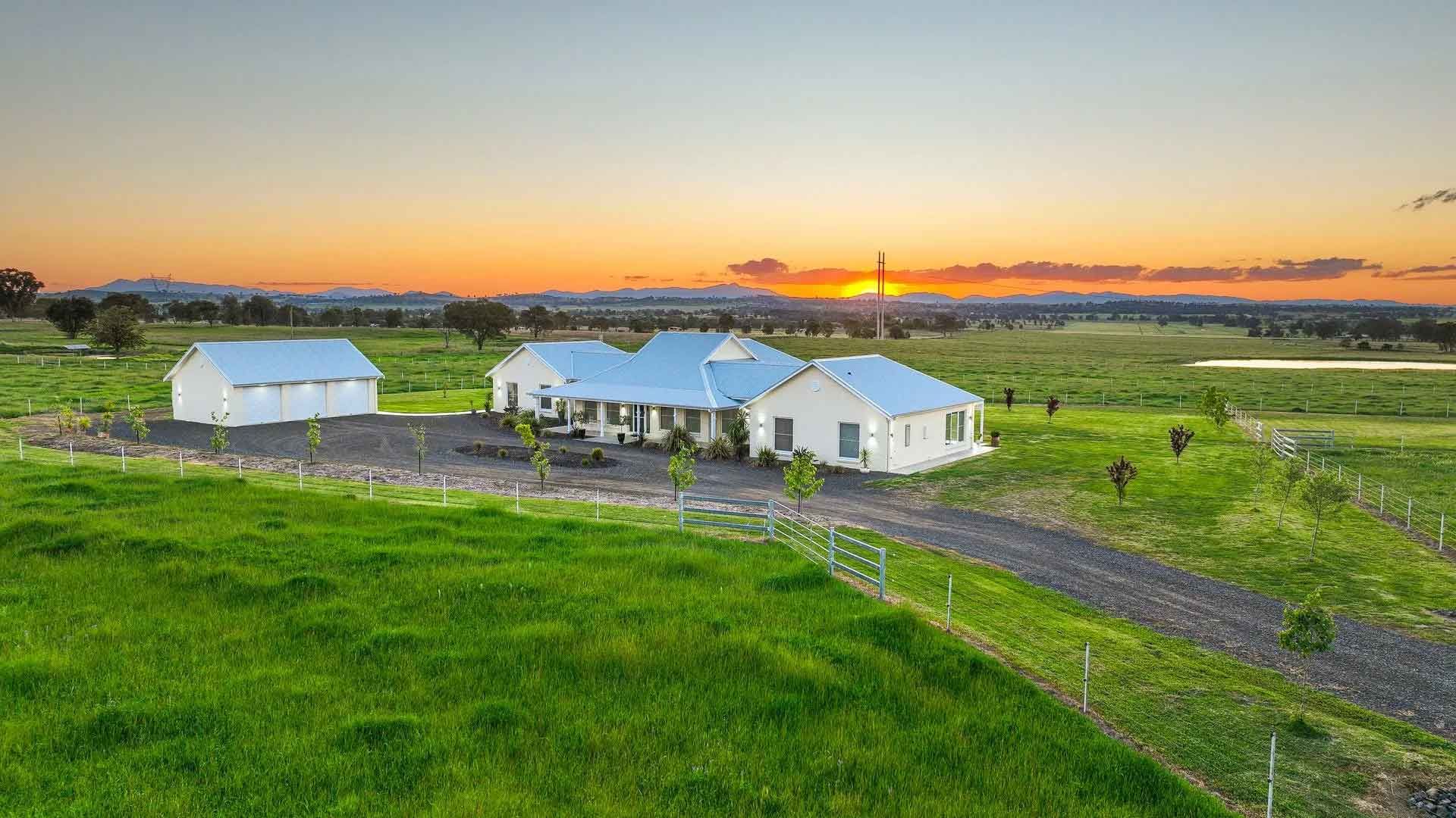 An aerial view of a house in the middle of a grassy field at sunset.