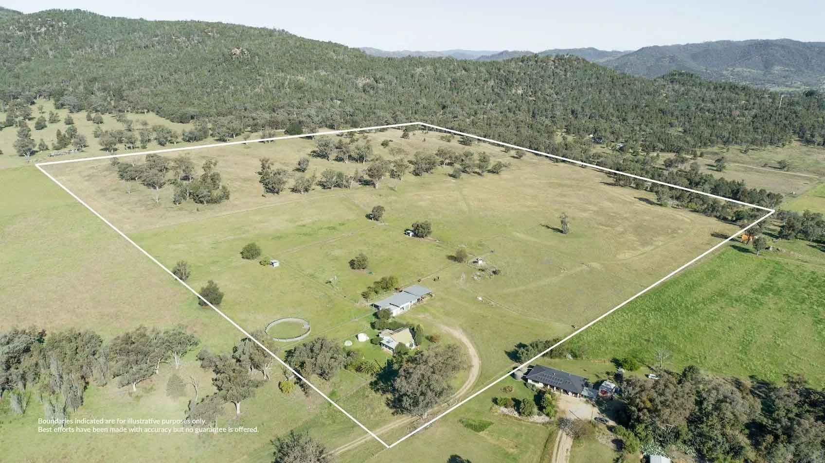 An aerial view of a large grassy field with a house in the middle of it.