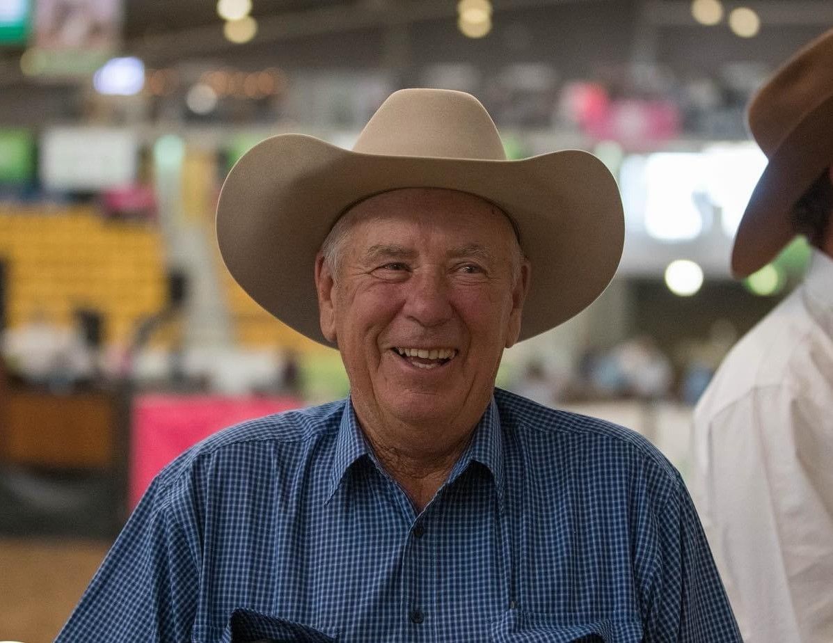 A man wearing a cowboy hat and plaid shirt is leaning against a truck.