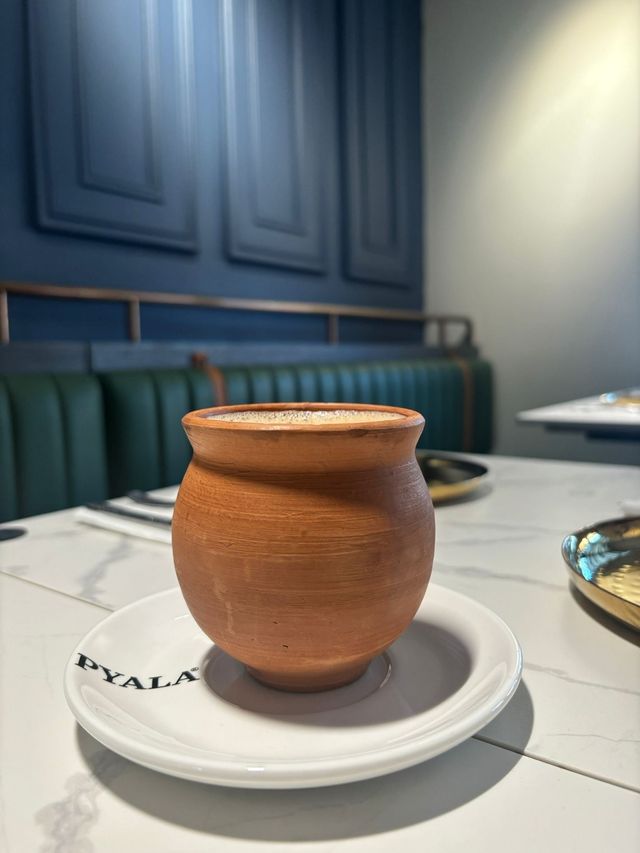A clay cup of chai on a saucer on a table, with blue and green booth seating in the background.