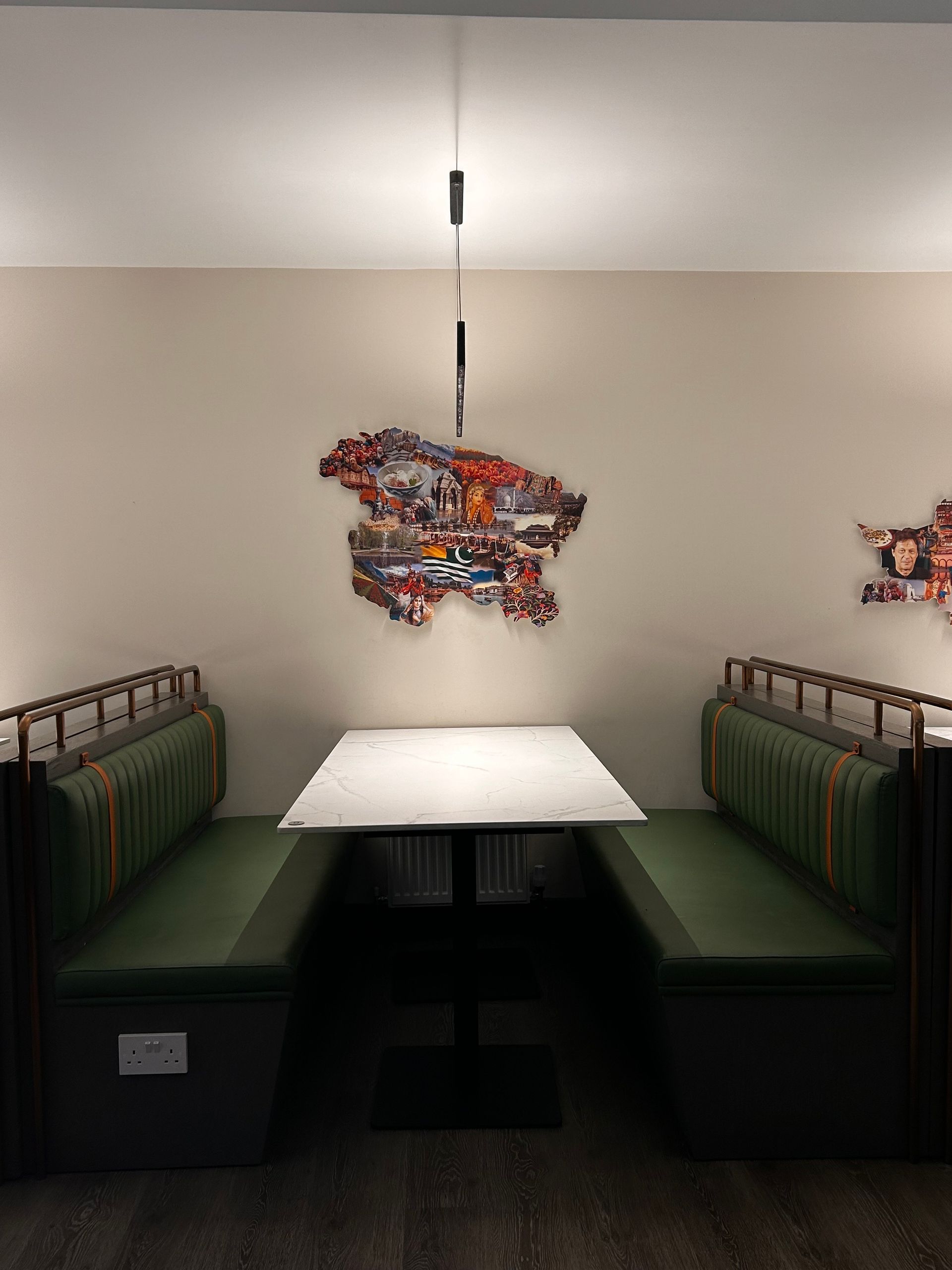 Booth seating in a restaurant, green cushions, white tabletop, artwork on the wall, modern lighting.