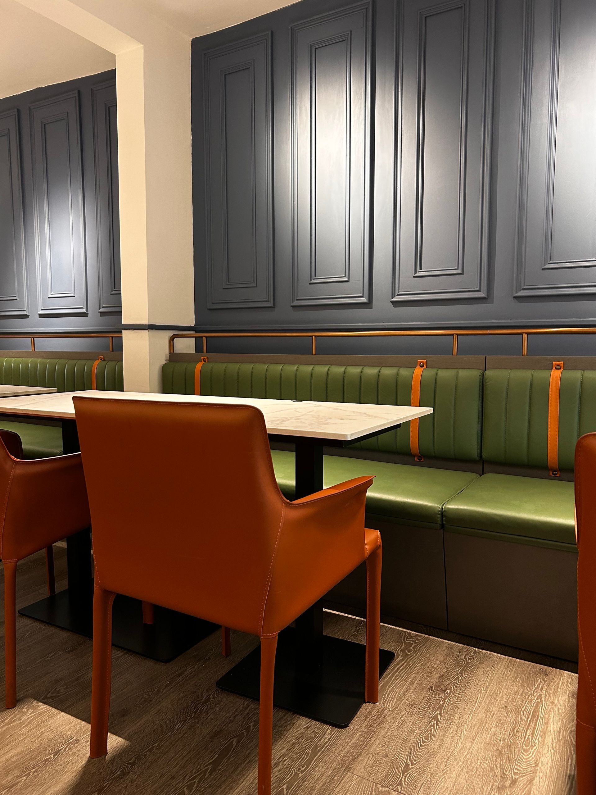Restaurant interior with a green booth, orange chairs, and a marble table against a blue paneled wall.