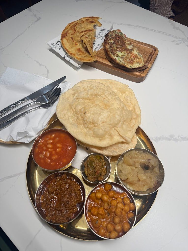 A South Asian breakfast platter with various curries, fried bread, and flatbreads on a white marble table.
