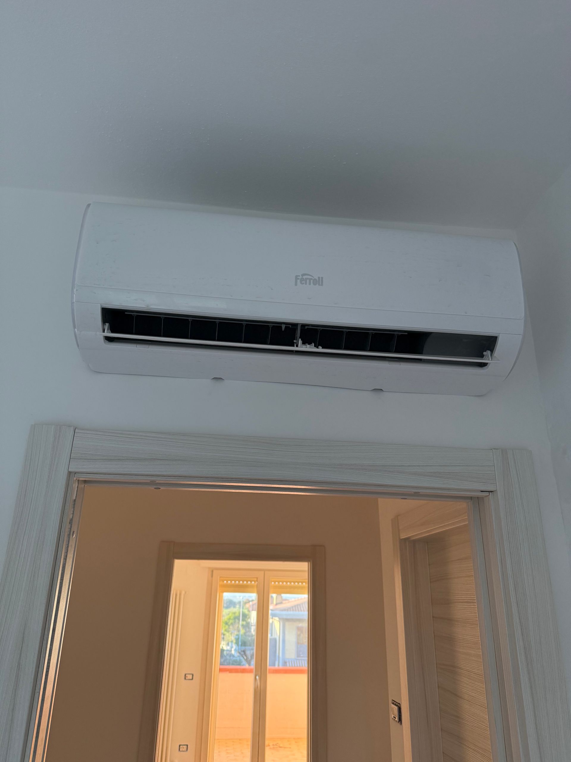 Un condizionatore d'aria bianco a parete installato sopra una porta che conduce a una stanza soleggiata.