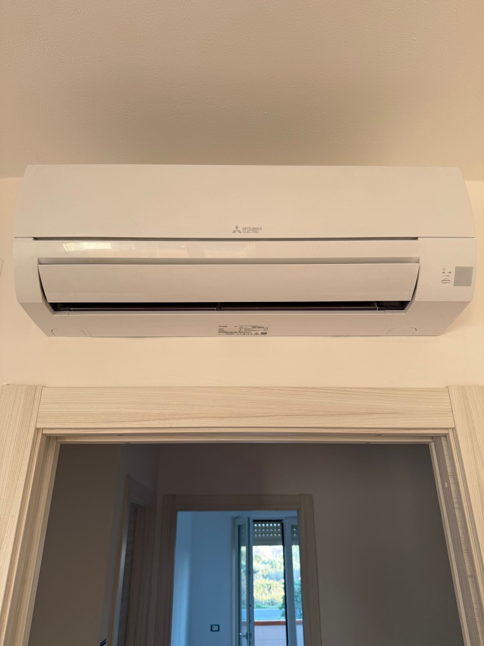 Un condizionatore d'aria Mitsubishi bianco a parete, posizionato sopra una porta che conduce a un'altra stanza.