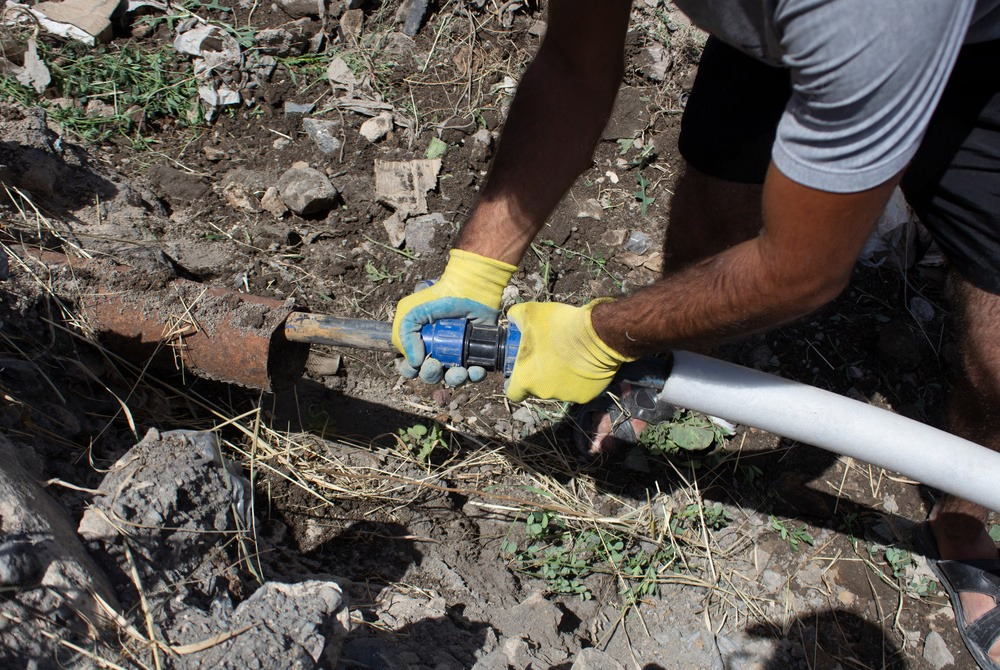 a man wearing yellow gloves is working on a pipe in the dirt .