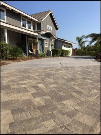 Gray brick driveway leading to a two-story gray house with white trim.