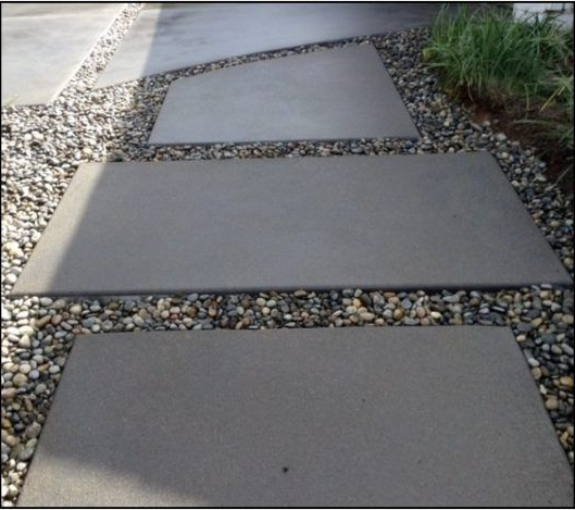 Gray concrete stepping stones set in a bed of pebbles, leading toward green plants.