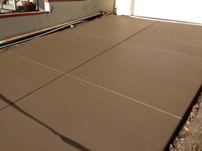 Freshly poured brown concrete driveway, with marked separation lines and garage entrance visible.