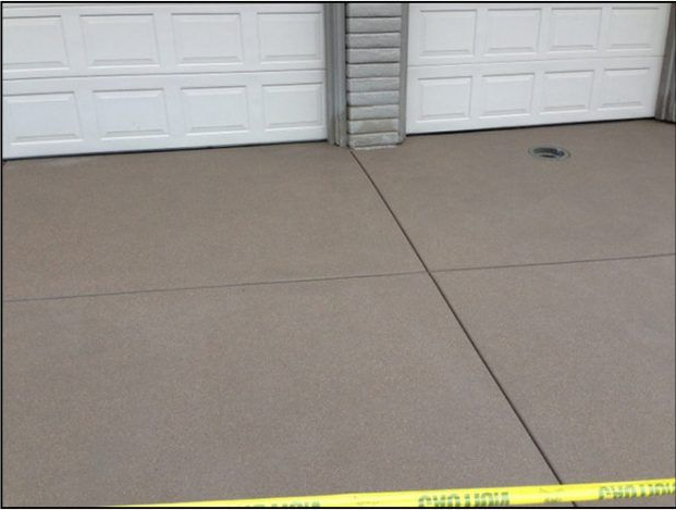 Gray concrete driveway with two white garage doors, a drain, and safety tape.