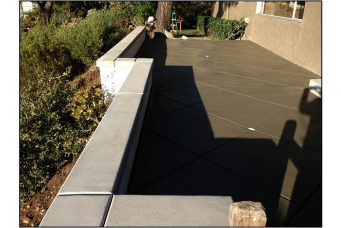 Newly poured concrete patio next to a retaining wall on a sloped yard.