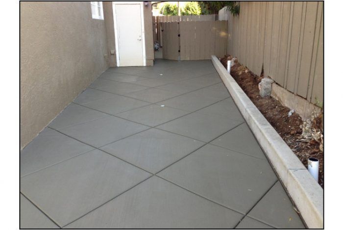 Concrete patio with a diagonal-line design next to a fence and building with a white door.