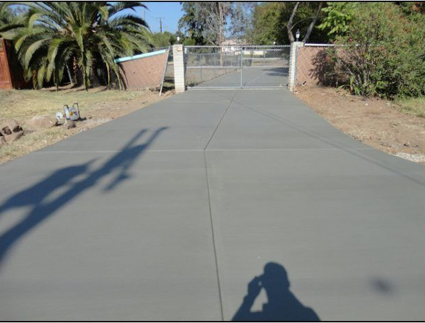A gray concrete driveway leads to a gated property, with a shadow in the foreground.