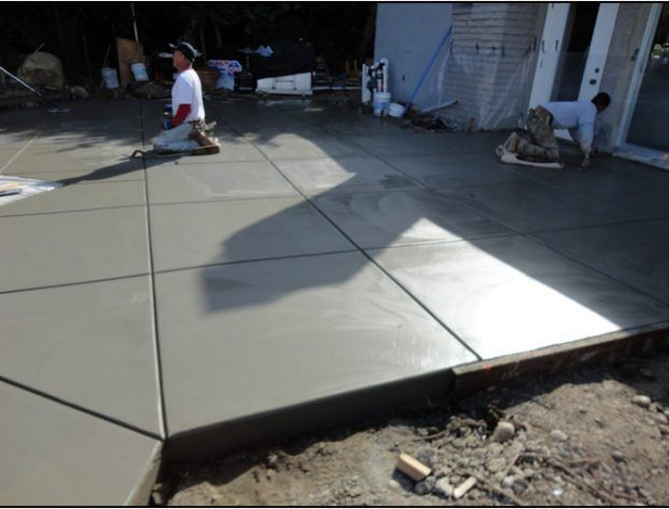 Construction workers kneeling, smoothing fresh concrete paving outdoors.
