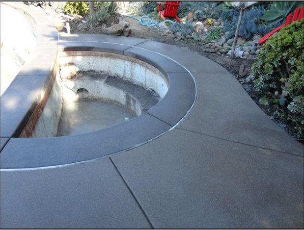 Concrete patio with curved border surrounding an empty, circular pool.