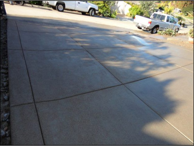 Concrete driveway with grid pattern, shadowed, and parked pickup trucks.