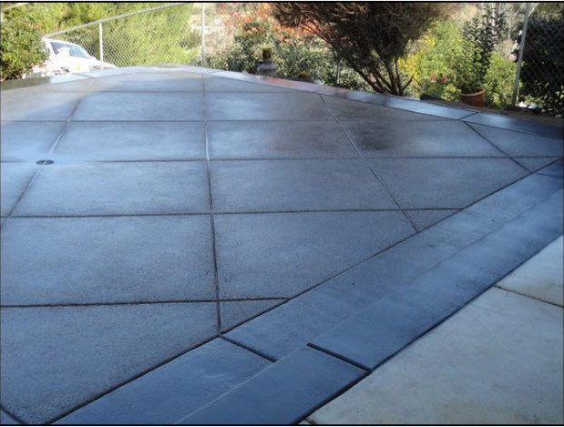 Gray concrete patio with dark border, wet surface, and surrounding greenery.