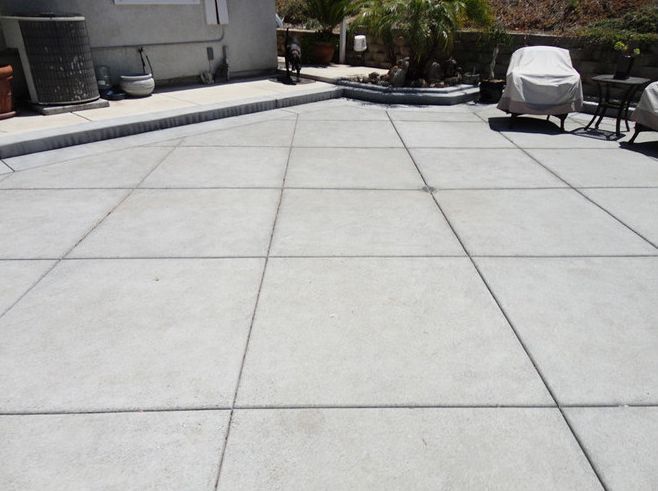 Large concrete patio with square grid pattern. Outdoor setting with potted plants, furniture.