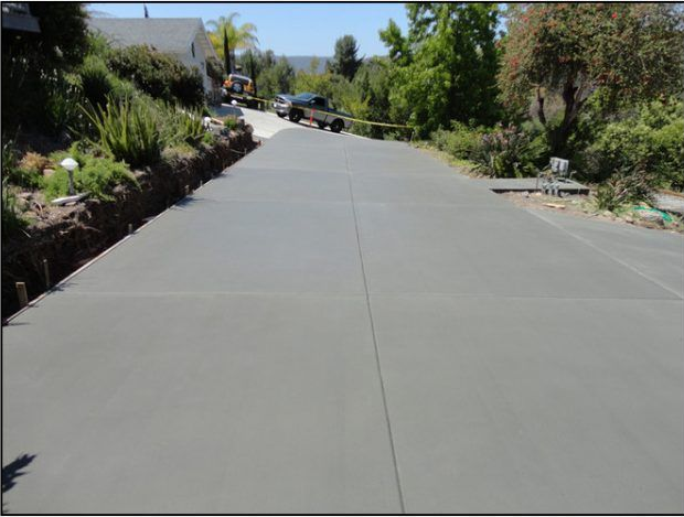 Newly poured concrete driveway, long and sloped, with construction vehicles and surrounding greenery.