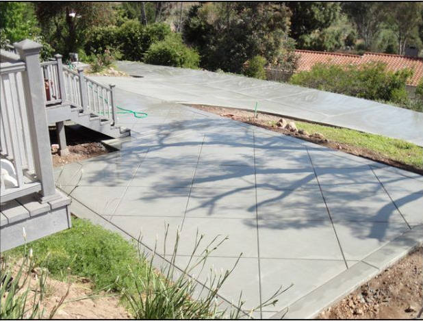 Concrete patio next to a wooden deck, shadows of tree branches.