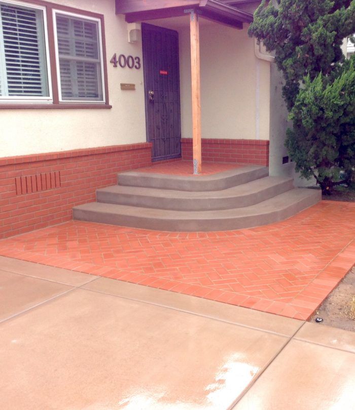 Exterior of a house with red brick details, a concrete walkway, and steps leading to the front door.