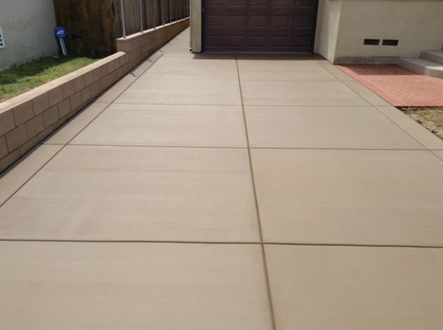 Concrete driveway with grid pattern, leading to a garage.  Tan colored concrete, brick retaining wall on the left.
