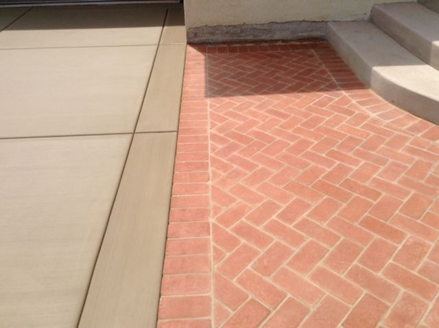 Concrete driveway next to red brick walkway leading to concrete steps.