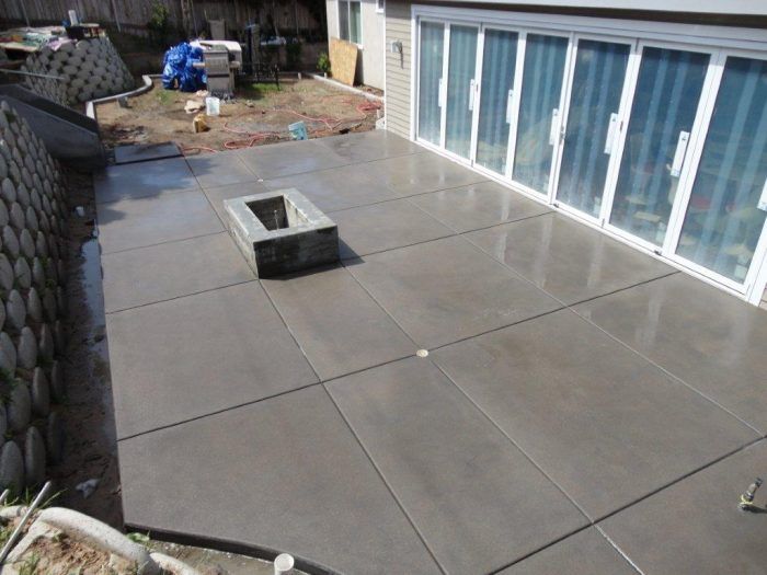 Concrete patio with fire pit, bordering house with glass doors, and retaining wall.