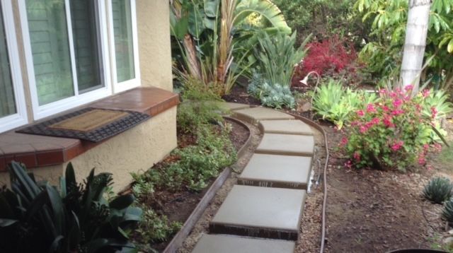 Stone path winds through a garden of green and red flowering plants.