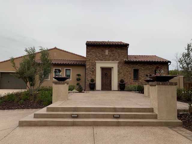 Tan stucco and brick home with terracotta roof. Entryway has raised platform, steps, and decorative bowls.