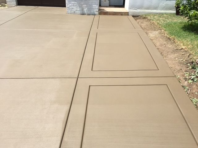 Newly poured concrete driveway and sidewalk with geometric design in a residential setting.