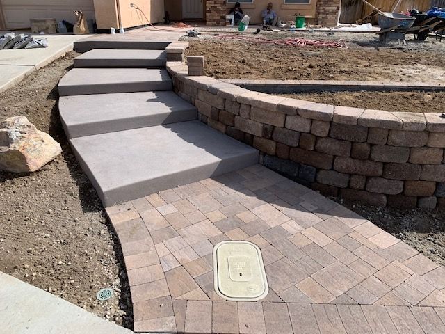 Stone pathway with steps leading to a house, next to a retaining wall and dirt yard.