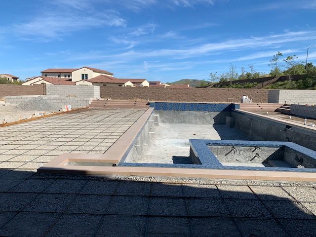 Construction site with a partially built swimming pool and surrounding concrete, under a blue sky.