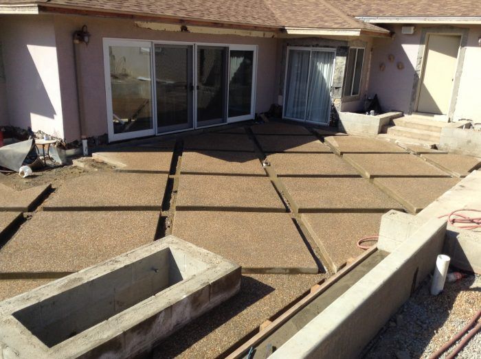 Patio with square concrete tiles being installed near a house with sliding glass doors.