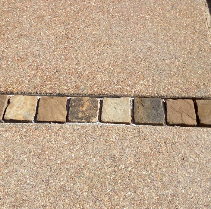 Tan speckled concrete with a decorative strip of square, earthy-toned tiles.