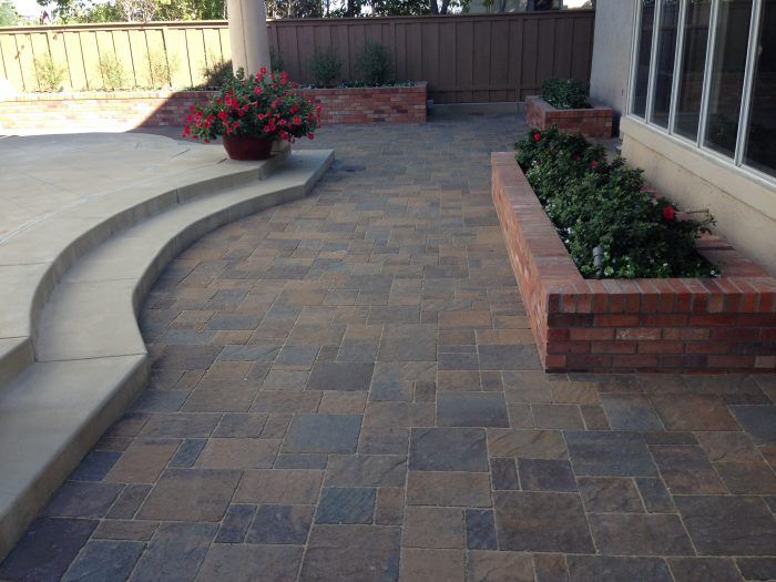Brick patio with brick planters and steps leading to a concrete patio area, flowers present.