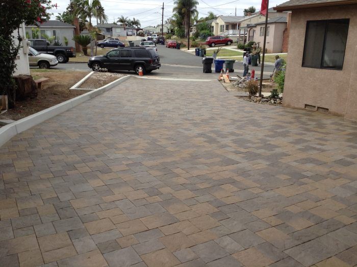 Brick paver driveway leads to a residential street; black SUV parked on the street.