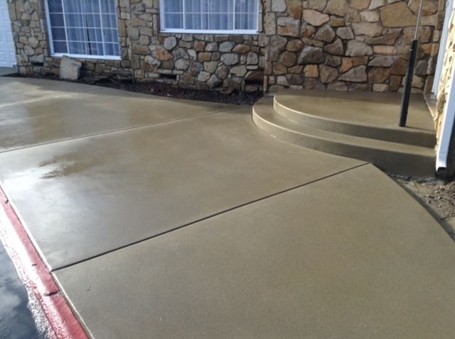 Freshly poured concrete sidewalk and steps in front of a stone building with windows.