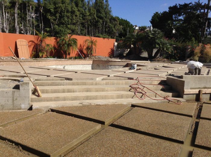 Construction site with concrete slabs, steps, and worker near a pool. Orange wall in background.
