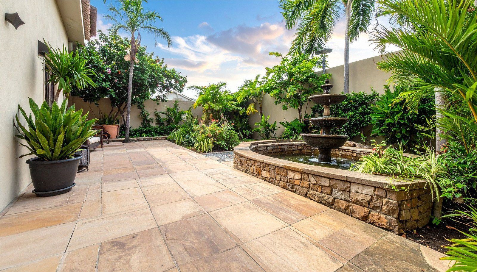 Patio with stone pavers, fountain, and lush tropical plants.