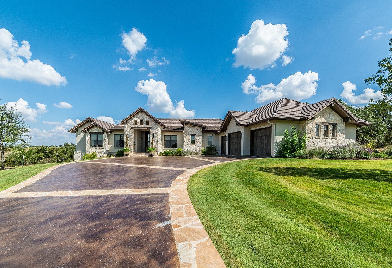 Luxurious stone house with brown roof and driveway on a bright sunny day.