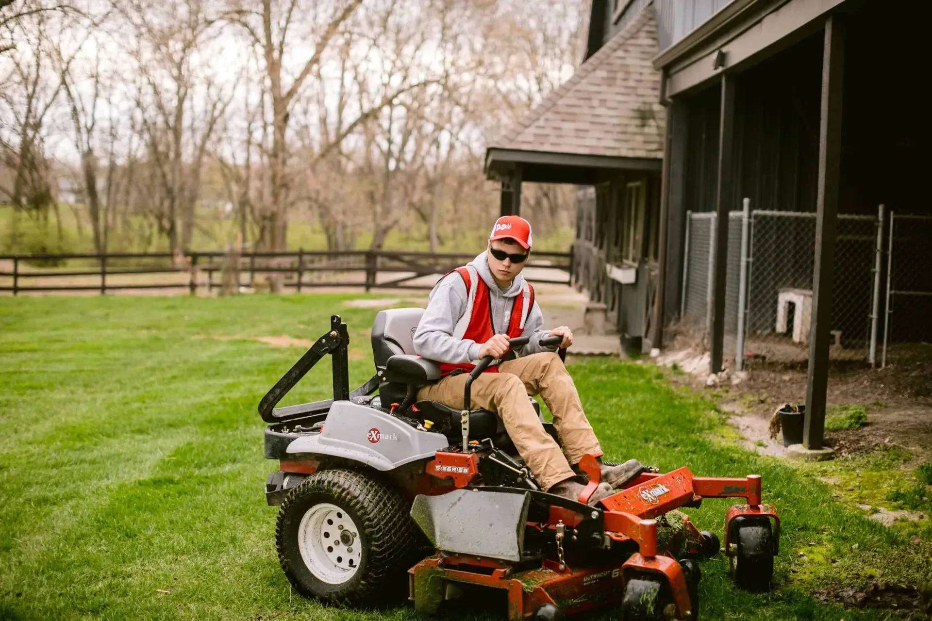 Man on a riding lawnmower mowing a green lawn near a house.