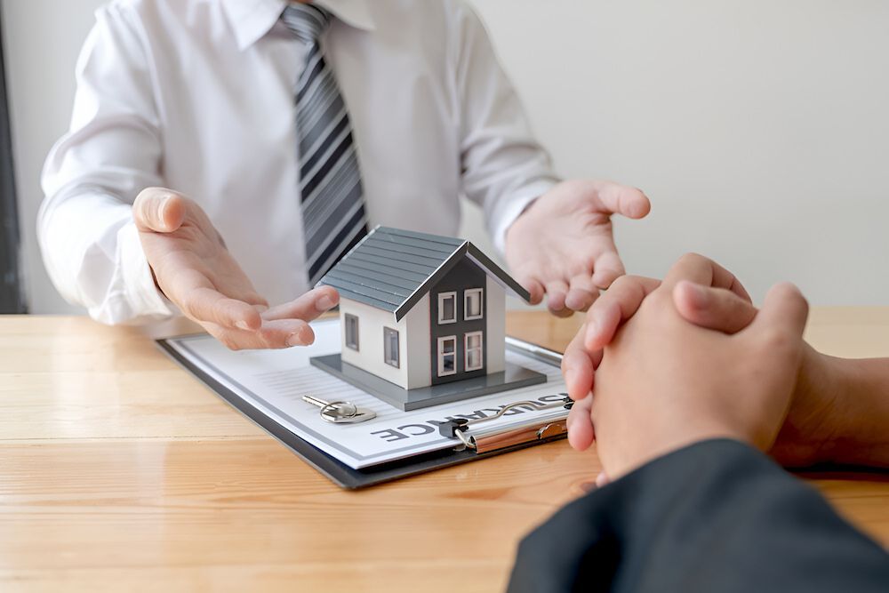 A Man Is Holding A Model House In His Hands While Sitting At A Table — Romy Sidhu Ray White Weir Views In Weir Views, VIC