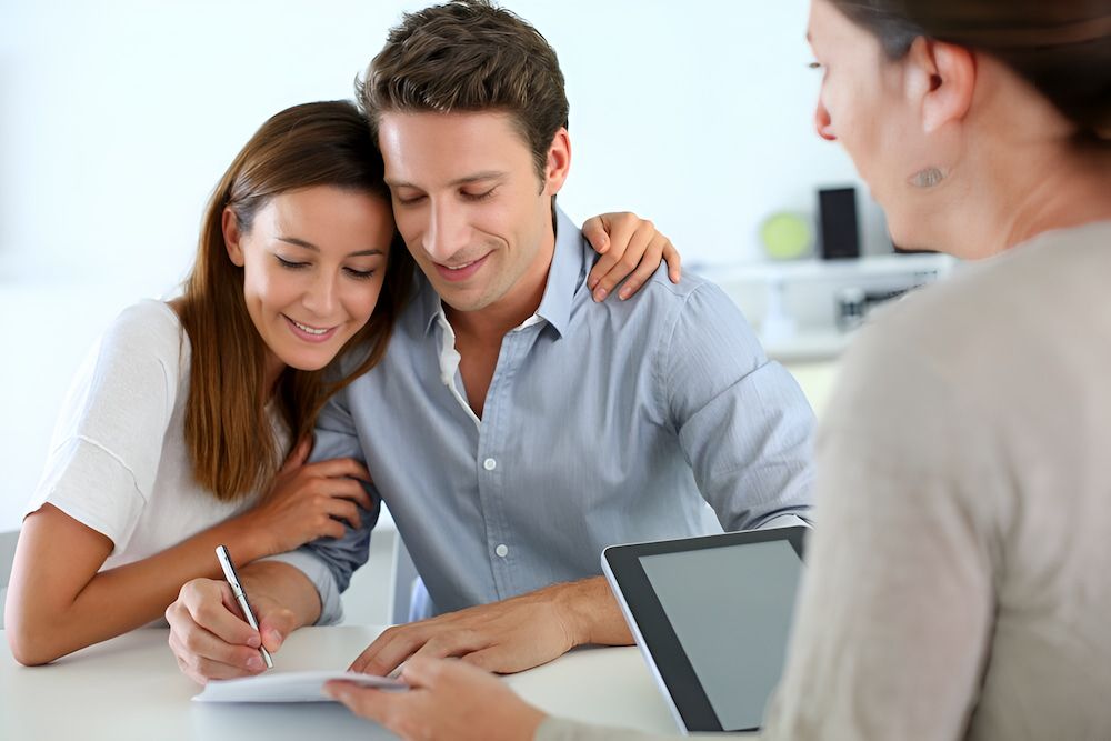 A Man And A Woman Are Sitting At A Table Signing A Document — Romy Sidhu Ray White Weir Views In Melton, VIC