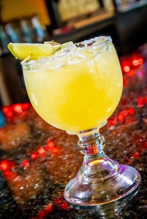 Cocktail in a glass garnished with an orange slice, set on a bar with blurred lights.