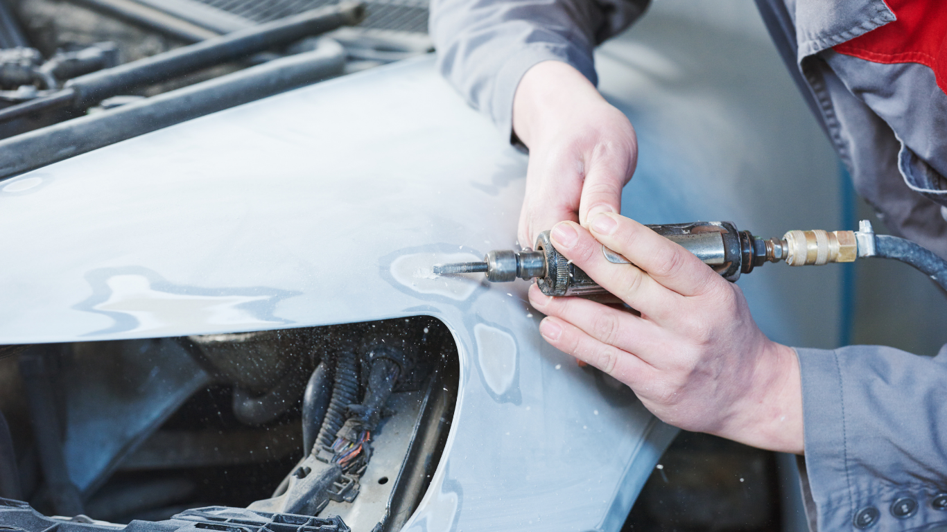 Mechanic using a pneumatic tool to sand a car fender.