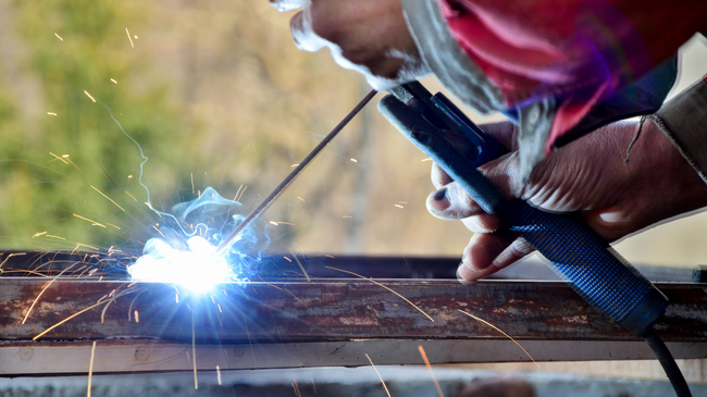 Welder using a welding torch on metal, creating sparks and bright light.