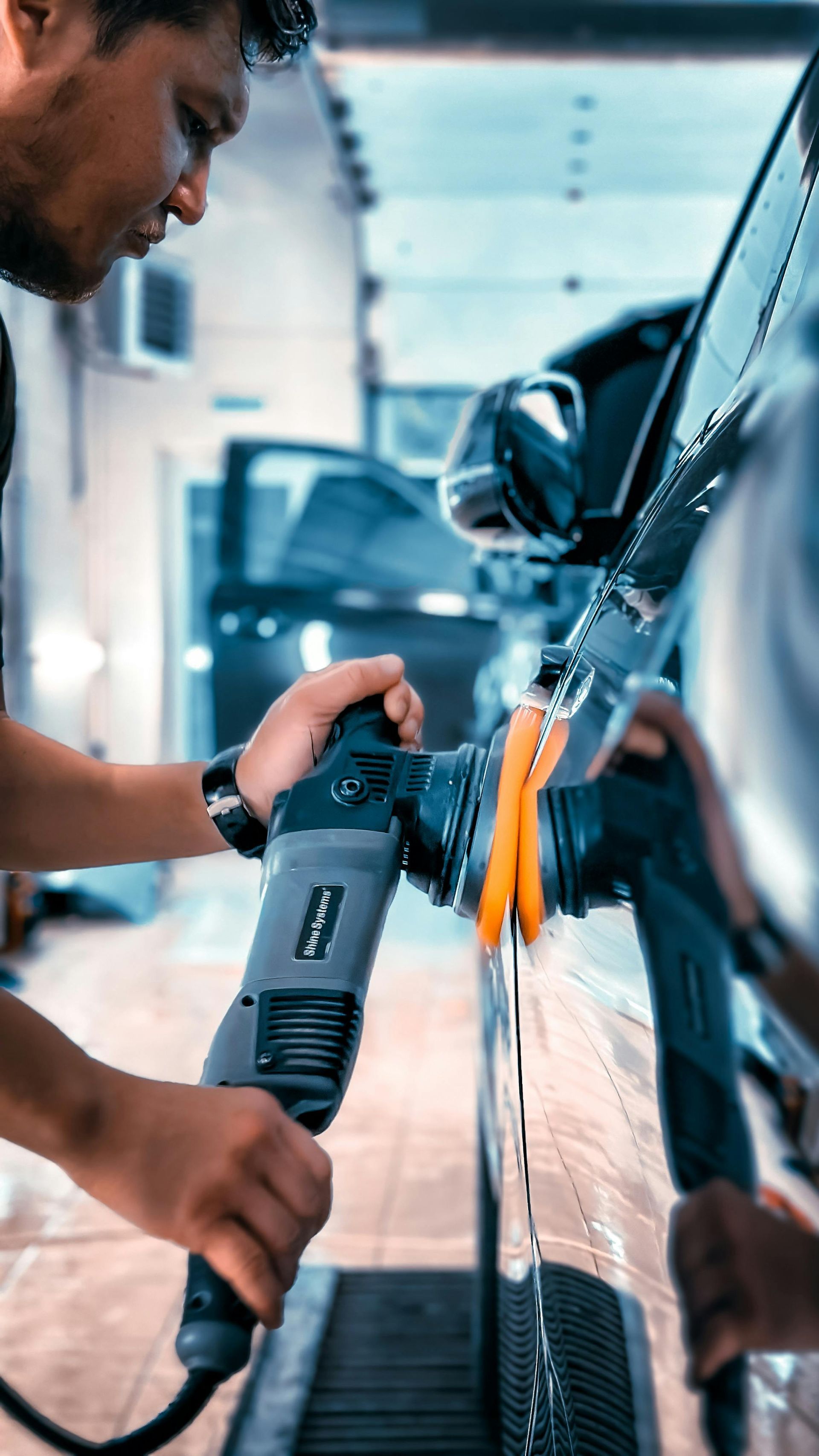Worker using a power tool to repair a black car in an auto body shop